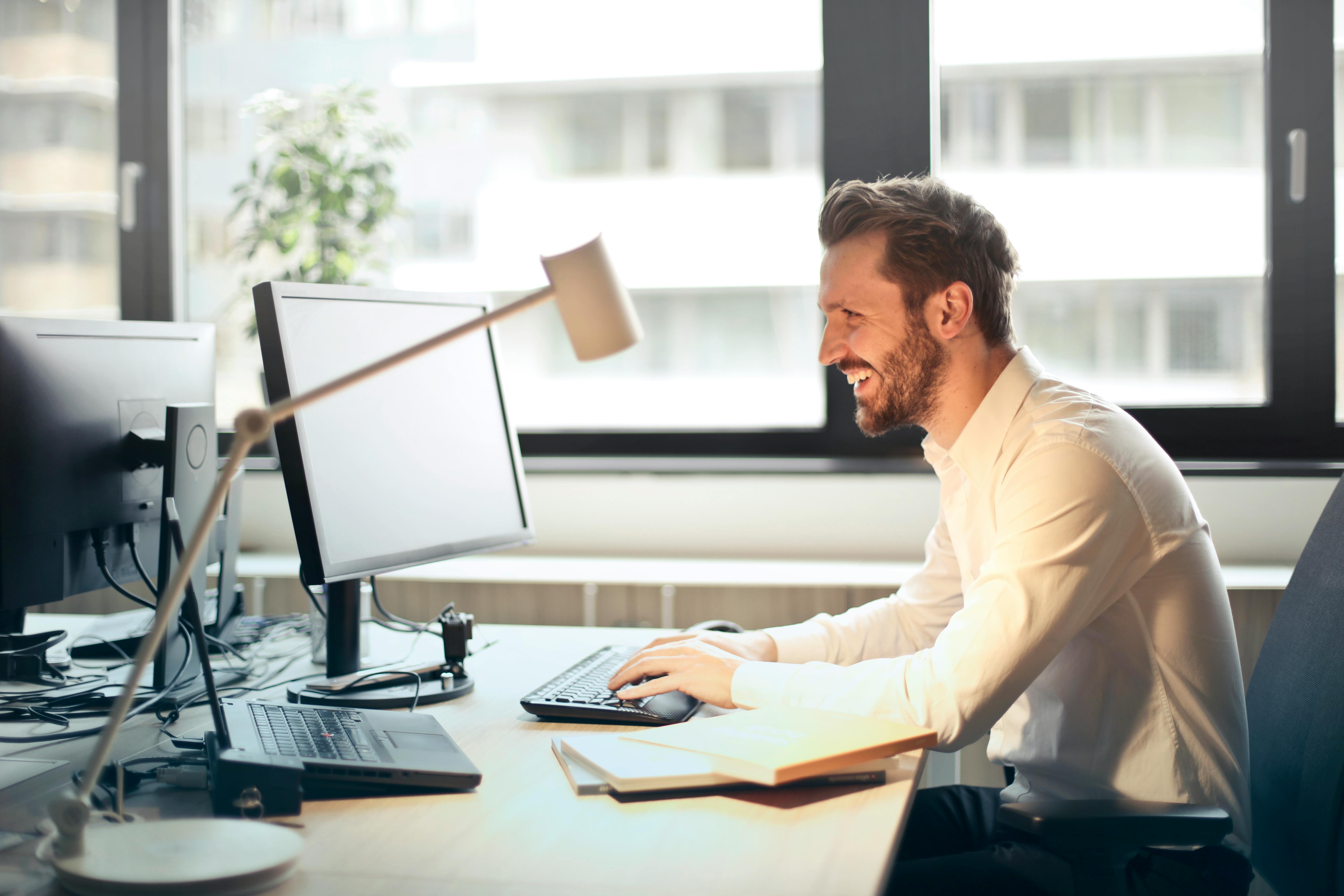 pexels-olly-840996 remote employee working at a desk with dual monitors in a modern office setting, tracking tasks and time